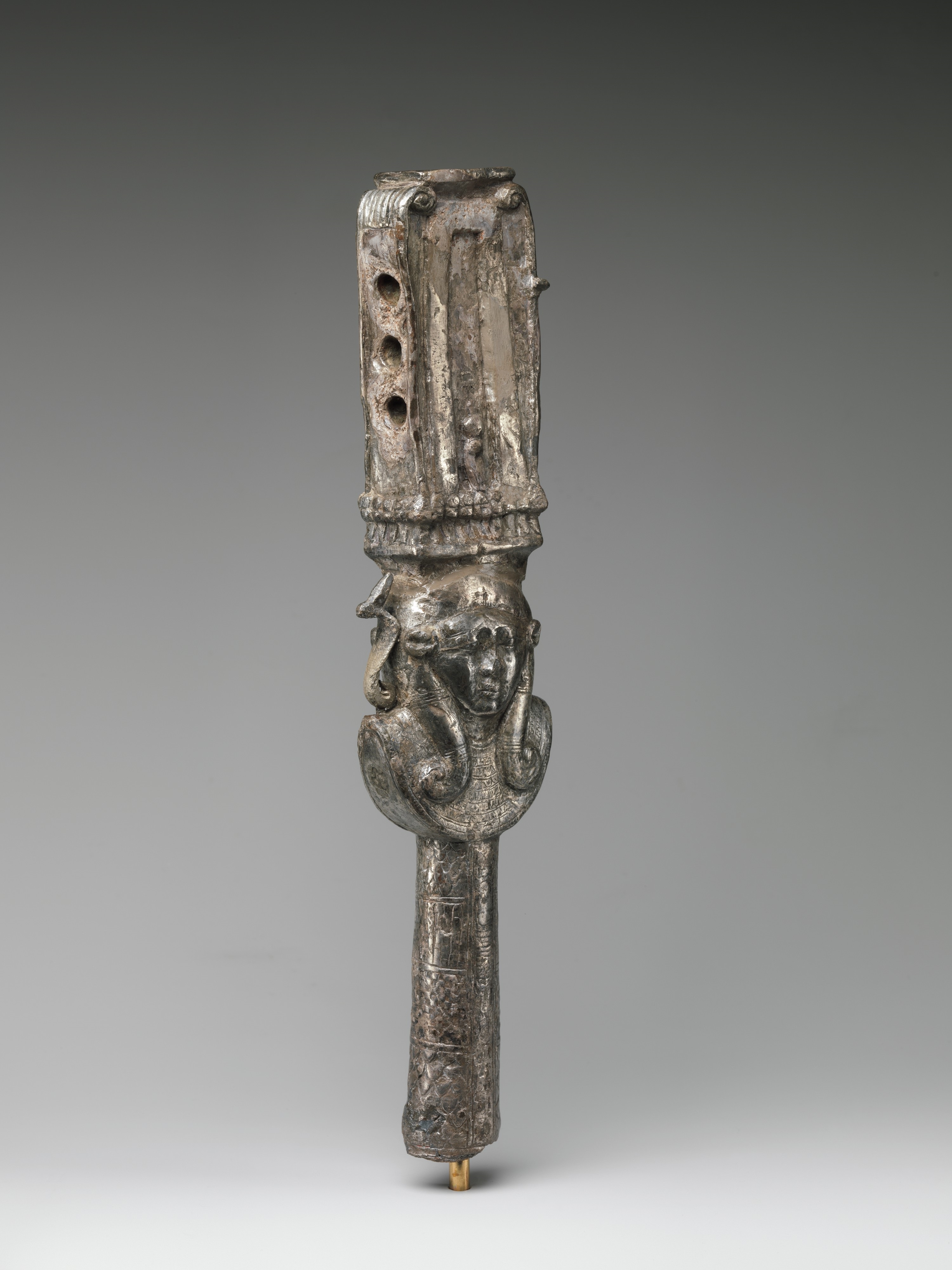 A silver Egyptian sistrum with a Hathor emblem beneath its shrine-shaped upper section.
